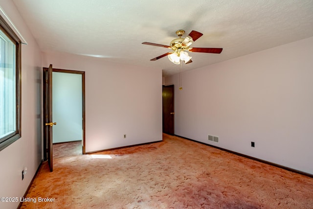 empty room with baseboards, visible vents, a ceiling fan, and light colored carpet