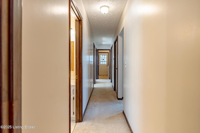 hallway with a textured ceiling, baseboards, and light carpet