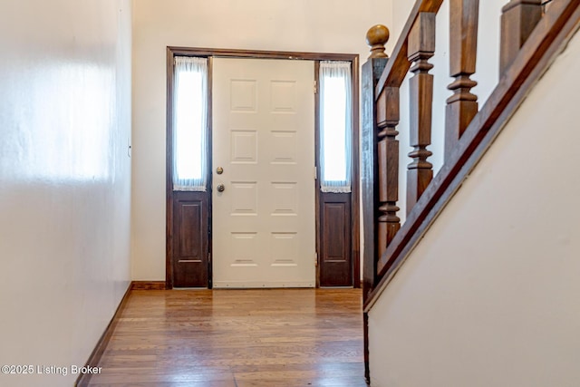 entryway featuring baseboards, wood finished floors, stairs, and a healthy amount of sunlight