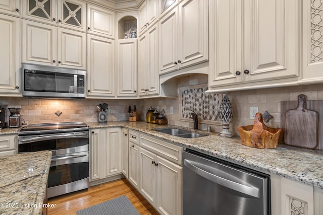 kitchen with light stone countertops, a sink, light wood-style floors, stainless steel appliances, and tasteful backsplash