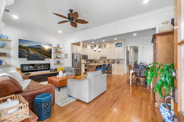living area with visible vents, a ceiling fan, light wood finished floors, and ornamental molding
