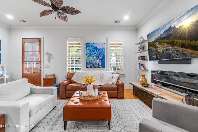 living area featuring crown molding, a ceiling fan, light wood-style flooring, and visible vents