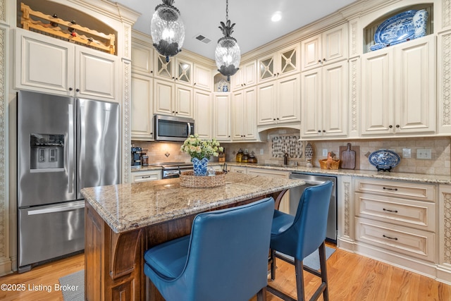kitchen with a kitchen island, light stone counters, light wood-style flooring, hanging light fixtures, and stainless steel appliances