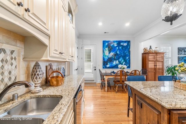 kitchen featuring ornamental molding, tasteful backsplash, light stone counters, a sink, and light wood-style flooring