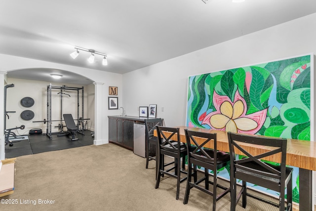 carpeted dining area with arched walkways, decorative columns, and a sink