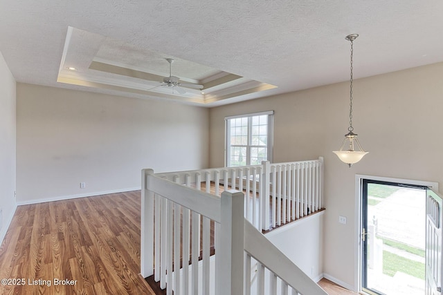 corridor with an upstairs landing, a tray ceiling, baseboards, a textured ceiling, and wood finished floors