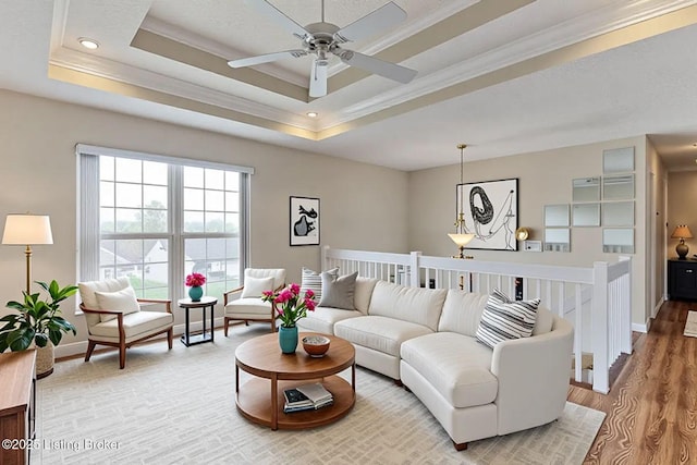 living area with a tray ceiling, a ceiling fan, baseboards, ornamental molding, and wood finished floors