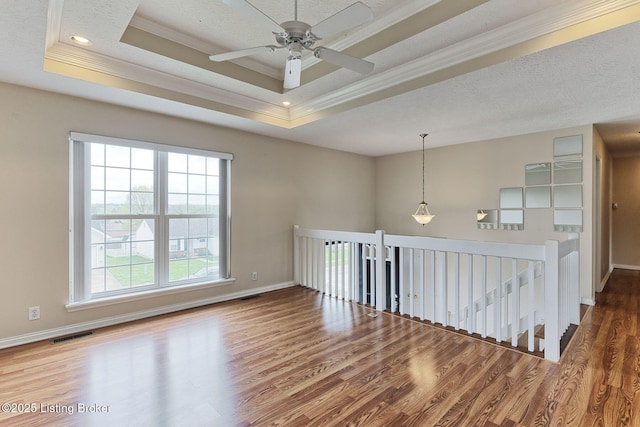 empty room featuring crown molding, a wealth of natural light, wood finished floors, and a tray ceiling