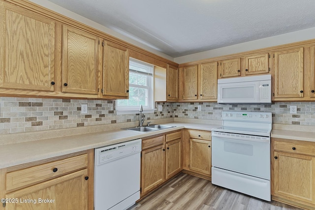 kitchen featuring white appliances, decorative backsplash, light countertops, a sink, and light wood-type flooring