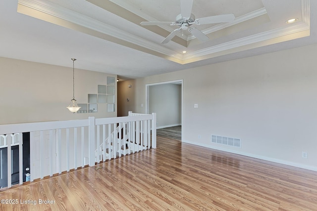 empty room featuring a ceiling fan, visible vents, baseboards, ornamental molding, and wood finished floors