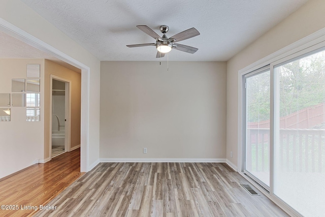 empty room with light wood-style floors, ceiling fan, baseboards, visible vents, and a textured ceiling