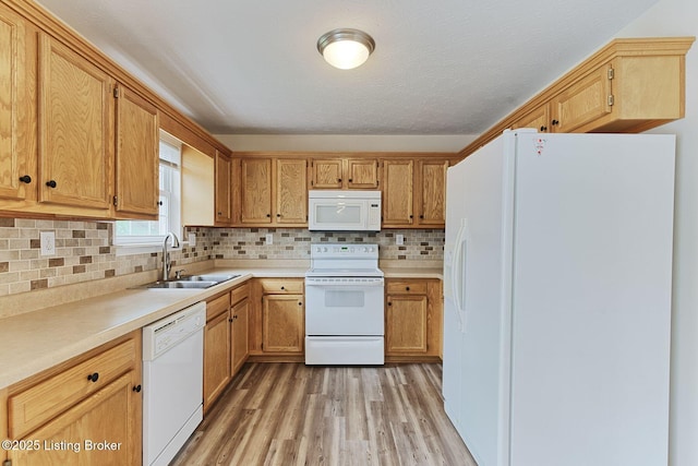 kitchen with white appliances, light wood-style flooring, decorative backsplash, light countertops, and a sink