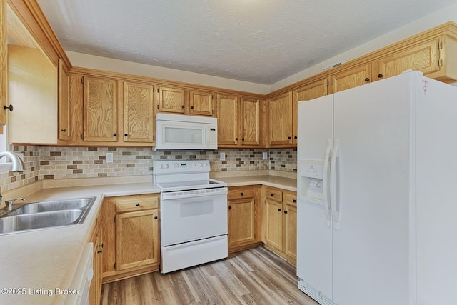 kitchen with light wood finished floors, a sink, decorative backsplash, white appliances, and light countertops