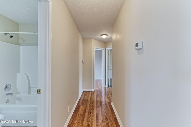 corridor with a textured ceiling, wood finished floors, and baseboards