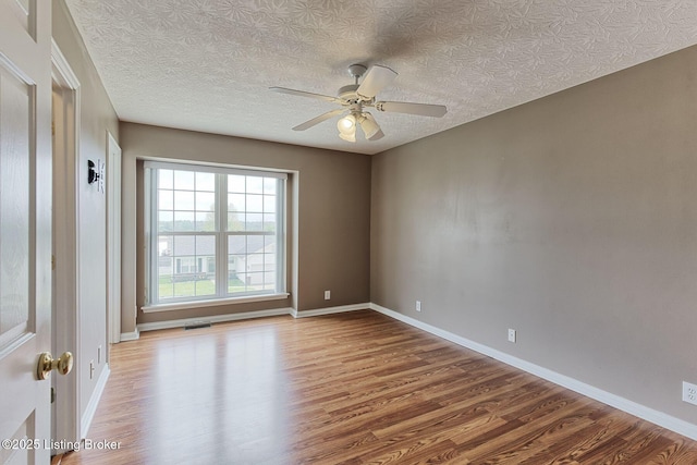 empty room with a ceiling fan, visible vents, baseboards, a textured ceiling, and wood finished floors