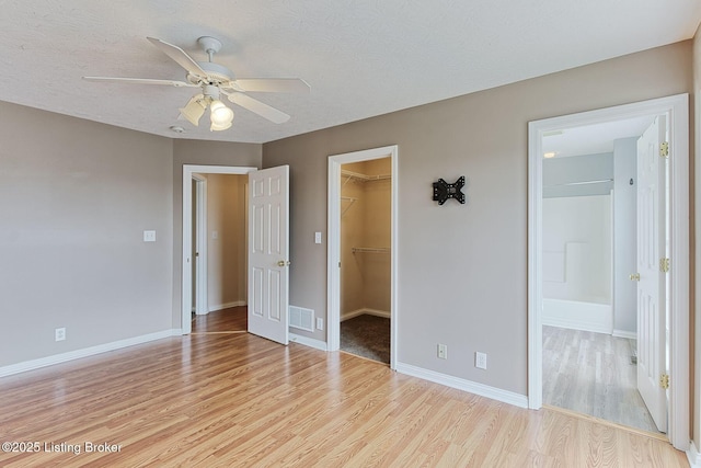 unfurnished bedroom with visible vents, light wood-style floors, a closet, baseboards, and a walk in closet