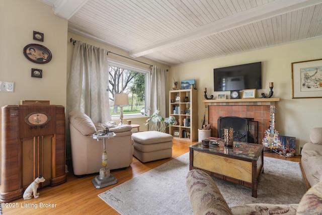 living area with a tiled fireplace, beam ceiling, wooden ceiling, and wood finished floors