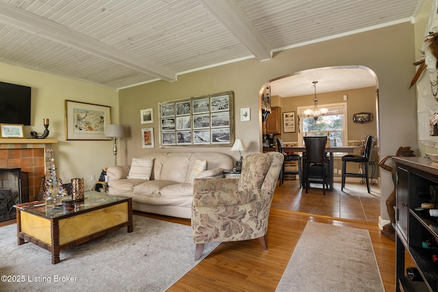 living room featuring arched walkways, a tile fireplace, a notable chandelier, and beam ceiling