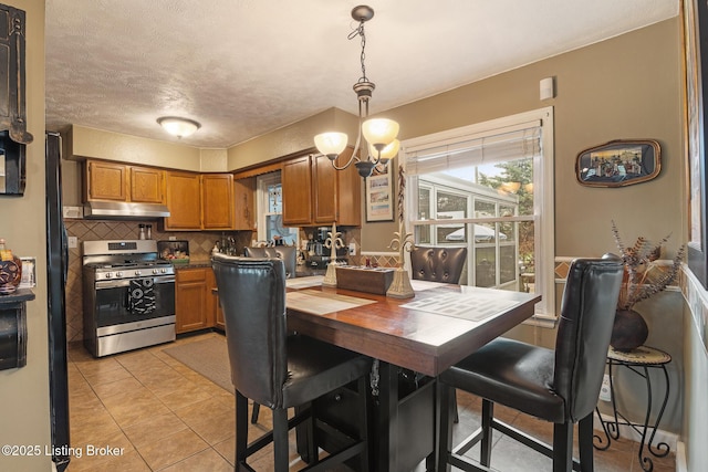 kitchen featuring tasteful backsplash, brown cabinetry, stainless steel gas range, a wealth of natural light, and under cabinet range hood