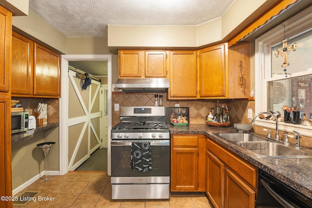 kitchen with under cabinet range hood, dark countertops, a sink, and appliances with stainless steel finishes