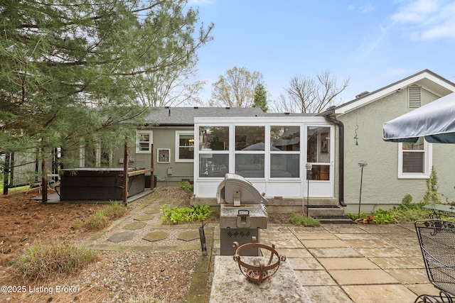 rear view of property with a sunroom, a hot tub, entry steps, a patio, and stucco siding
