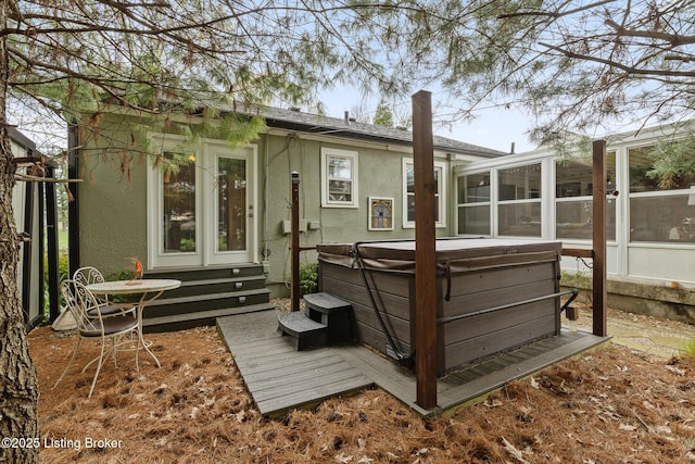 back of property with a sunroom, stucco siding, and a hot tub