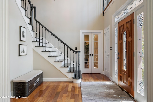 entryway featuring a high ceiling, french doors, stairway, and wood finished floors