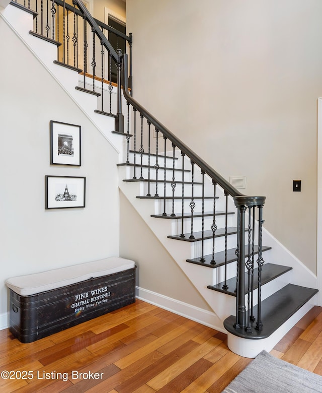 stairs featuring a towering ceiling, visible vents, wood finished floors, and baseboards
