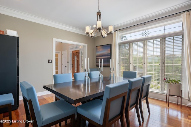 dining room with ornamental molding, light wood-style flooring, a chandelier, and baseboards