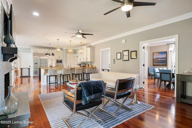 living room featuring dark wood-style flooring, ceiling fan, crown molding, and a brick fireplace