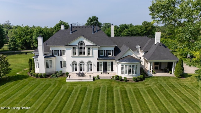 rear view of house featuring a patio, a chimney, and a lawn
