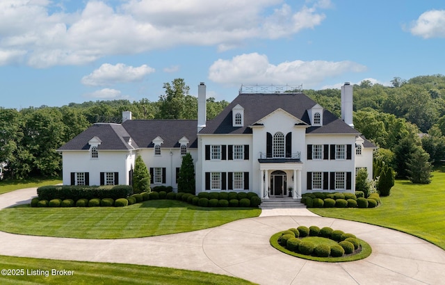 view of front of home featuring a front yard, a chimney, curved driveway, and stucco siding