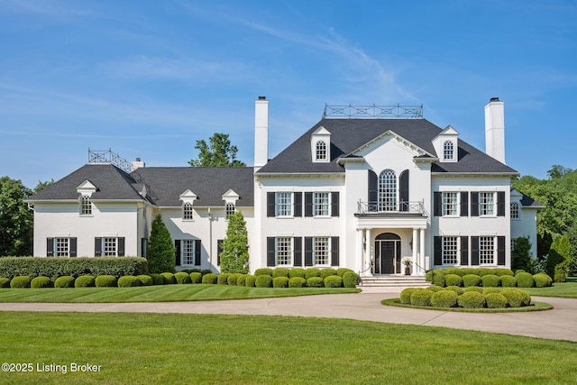 view of front of property featuring a balcony, a front yard, a chimney, and stucco siding