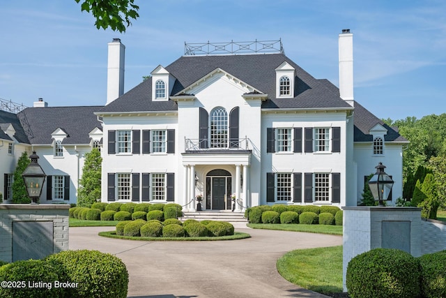 view of front of house featuring a balcony, a chimney, stucco siding, and curved driveway