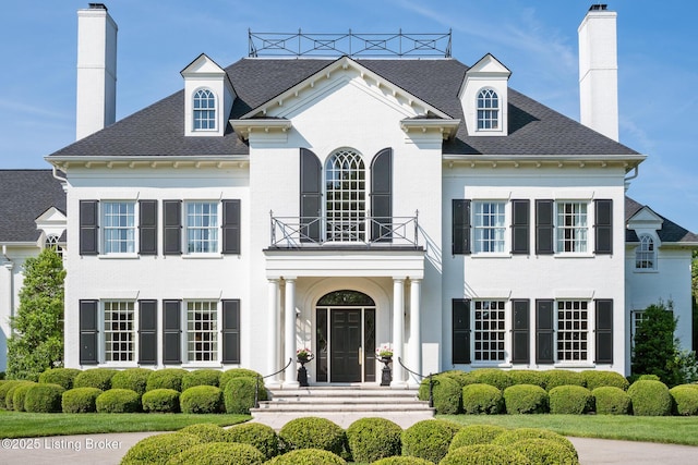 view of front of house featuring a balcony, a chimney, and a shingled roof
