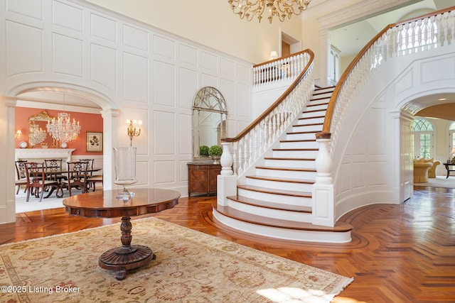foyer entrance with a chandelier, a decorative wall, arched walkways, decorative columns, and a high ceiling