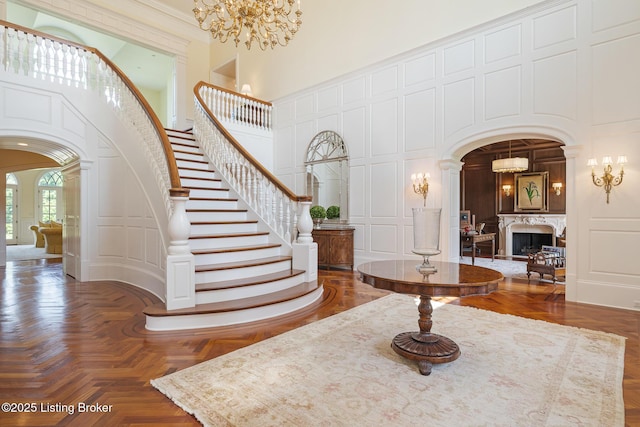 entryway featuring arched walkways, a decorative wall, a towering ceiling, stairway, and a fireplace