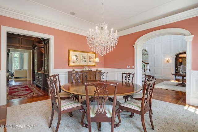 dining room with a decorative wall, arched walkways, ornamental molding, a chandelier, and a wainscoted wall