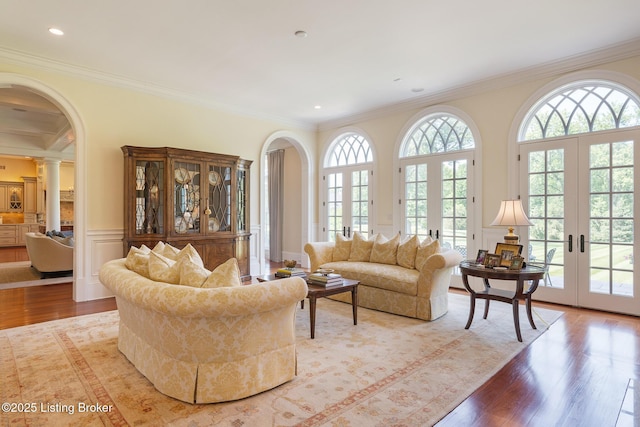 living room featuring wood finished floors, crown molding, french doors, ornate columns, and arched walkways