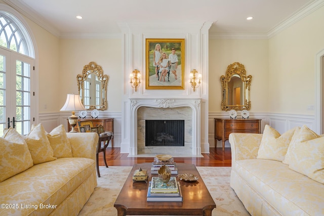 living area featuring crown molding, a wainscoted wall, a premium fireplace, a decorative wall, and wood finished floors