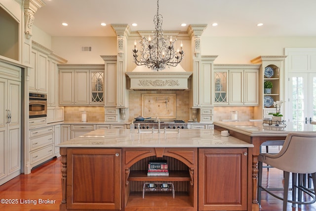 kitchen featuring a kitchen breakfast bar, recessed lighting, cream cabinetry, a chandelier, and glass insert cabinets