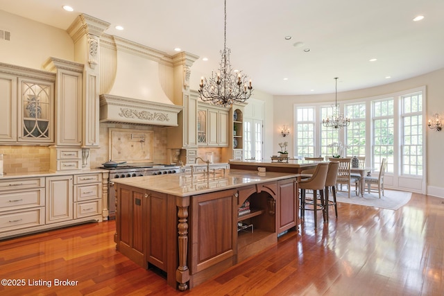kitchen featuring a chandelier, cream cabinetry, custom exhaust hood, high end range, and recessed lighting