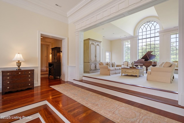 living room featuring wood finished floors, wainscoting, ornamental molding, and a decorative wall