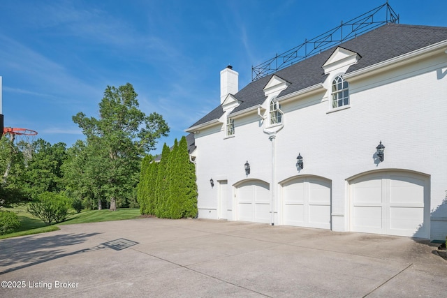 view of property exterior with concrete driveway, a chimney, a garage, and a shingled roof