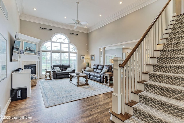 living room featuring wood finished floors, stairway, ceiling fan, visible vents, and a high ceiling
