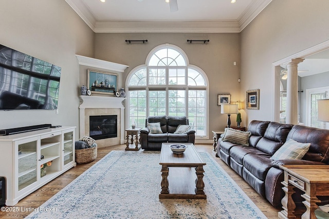 living room with a tiled fireplace, wood finished floors, decorative columns, ornamental molding, and a towering ceiling
