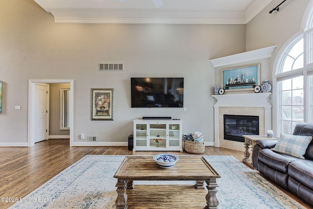 living room featuring wood finished floors, visible vents, crown molding, and a high ceiling