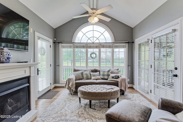living area featuring baseboards, ceiling fan, a fireplace, and vaulted ceiling