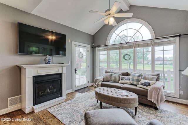 living area with beamed ceiling, ceiling fan, a fireplace, baseboards, and visible vents