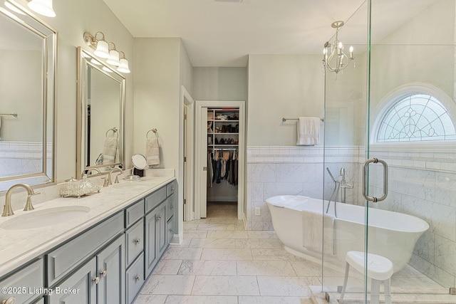 full bath featuring double vanity, tile walls, a walk in closet, and a sink